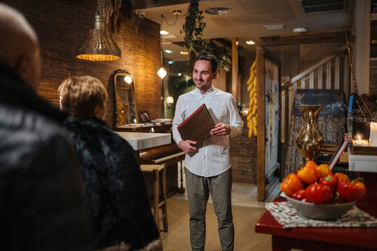 Smiling man with menu inviting couple to restaurant