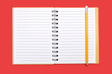 An open notebook with a binding and a yellow pencil on a red background. Open notepad with blank...