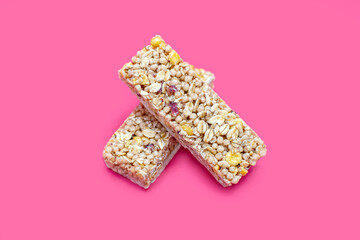 Two muesli bars on a pink background in the center of the image. Healthy sweet dessert snack. Cereal muesli with nuts, oatmeal and berries on a yellow background. Delicious and healthy dessert