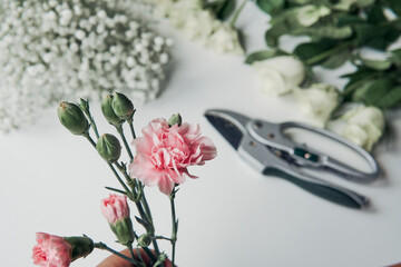 carnation with white roses, leaves and scissor on the table. making bouquet at home.