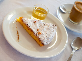 Slice of Spanish almond pie Tarta de Santiago sprinkled with sugar powder accompanied by coffee with milk and glass of sweet wine. Traditional serving of popular dessert