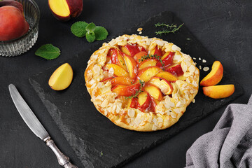Homemade tart peach galette open pie with fresh organic fruits, dark background with peaches. Close up view. Dark moody, low key shot.
