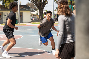 Diverse teenagers playing basketball together at a neighborhood park