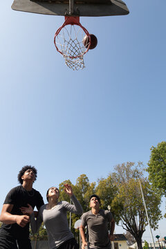 Diverse teenagers playing basketball together at a neighborhood park