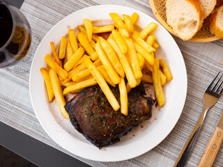 Deep-fried pork chop is on round plate.Meat richly seasoned with herbs and garnished with French fries, served with red wine