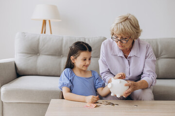 Obraz na płótnie Canvas Grandmother and her granddaughter Putting Coin Money In Piggybank At Home. Personal Savings, Bank Safety And Financial Investments Concept