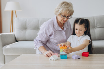 Naklejka premium Grandmother playing a board game with granddaughter, sitting in the living room, smiling while having a great time together.