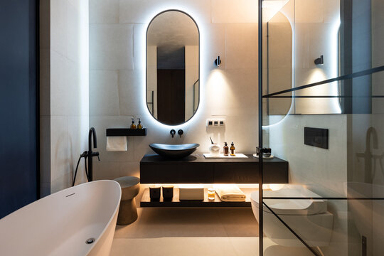 Big bathroom with backlight rounded mirror, shower and bathtub.