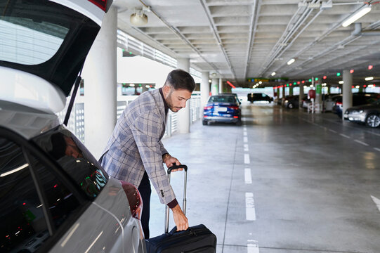 Man taking luggage from a car in an airport parking lot