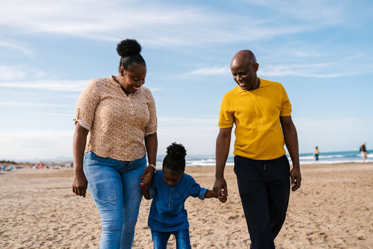 Happy black family holding hands and walking on beach