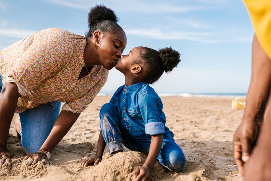 Black girl kissing mom on sandy beach