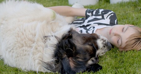 Relaxed boy lies on the grass with a dog in the village. He spends time without the Internet,...