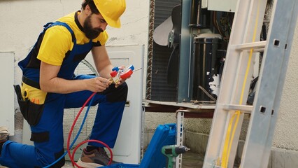 Expert technician commissioned for annual air conditioner maintenance, assembling manometer before starting work. Proficient worker checking freon leaks leading to reduced cooling efficiency