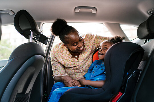 Content mother fastening daughter in baby seat