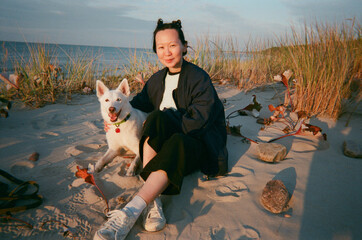 a woman sitting on a beach with a white dog 