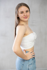 Portrait of young girl in tank top and jeans on a gray background
