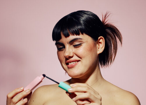 Happy Woman opening mascara brush over pink background
