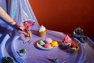 Hands of a young woman holding cocktail glass with sweet cakes