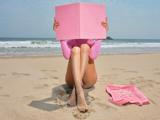 Woman covering her face with a pink book on the beach