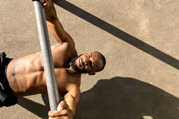 A young man pulls himself up on a horizontal bar on the workout area.
