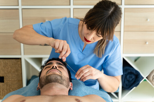 Female beautician plucking eyebrows for male client.