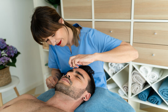 Female beautician plucking eyebrows for male client.