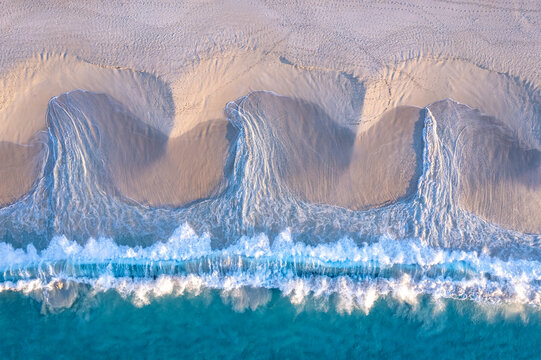 Aerial view of turquoise waves creating patterns in the sand
