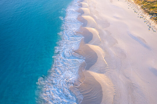Aerial view of turquoise ocean creating patterns in the sand at sunset