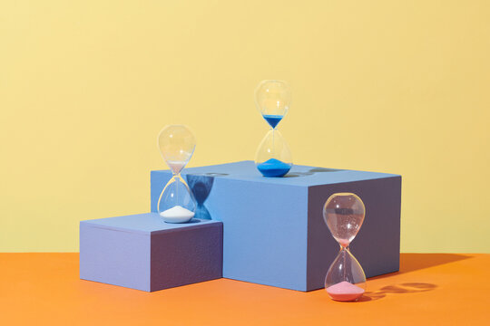 three hourglasses with color sand standing on blue podium