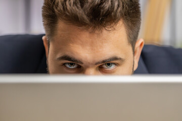 Close-up confident businessman hiding behind laptop computer, looking at camera, spying his...
