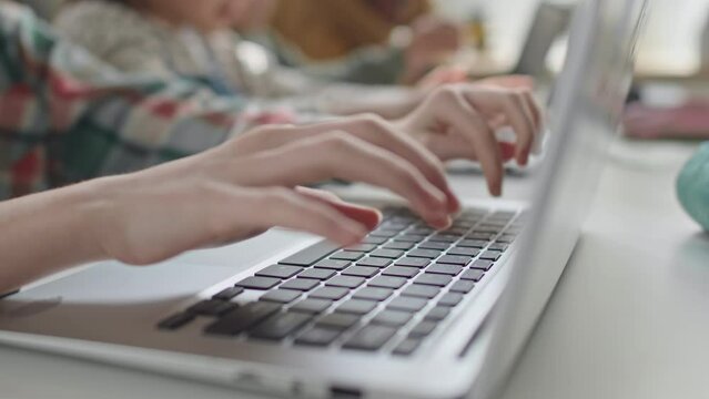 Close up impersonal shot of hands of girl typing on laptop keyboard at school desk during computer class