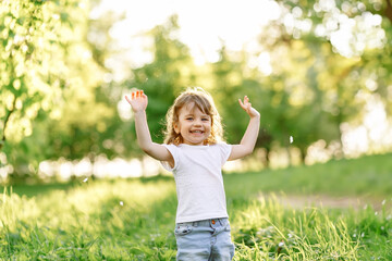 Happy little girl child having fun raising her hands up in sunny summer day