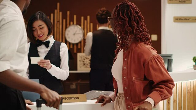Tourists finishing vacation trip, handing out room card key to cheerful friendly receptionists during check out process. Happy guests preparing to leave hotel after nice stay