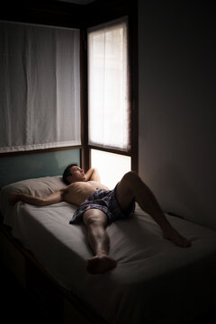 Lazy young man lying on bed looking through window