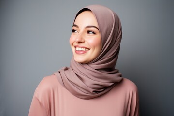 Portrait of a beautiful young muslim woman in hijab smiling on grey background