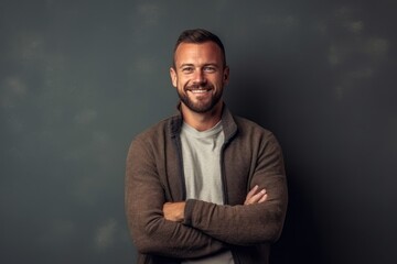 Obraz premium Portrait of a smiling young man standing with arms crossed against grey background