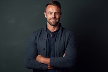 Handsome man standing with crossed arms against chalkboard background.