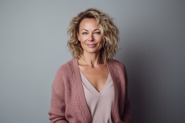 Fototapeta premium Portrait of a beautiful blonde woman with curly hair in a pink sweater on a gray background