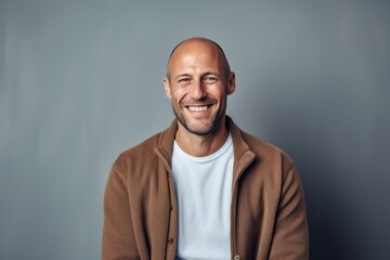 Fototapeta premium Portrait of a handsome young bald man smiling at the camera while standing against grey background