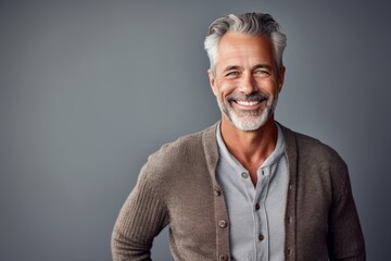 Obraz premium Handsome mature man is smiling and looking at camera while standing against grey background