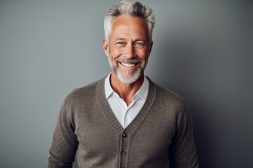 Obraz premium Portrait of a handsome senior man smiling and looking at camera while standing against grey background