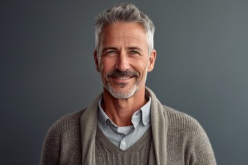 Fototapeta premium Portrait of a handsome mature man smiling at the camera while standing against grey background