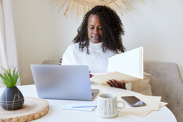 Mature Black woman paying bills online on computer and phone at home
