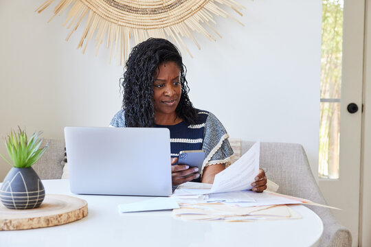 Mature Black woman paying bills and finances on computer and phone