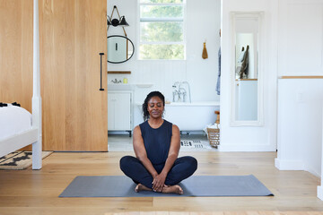 Mature Black woman meditating in yoga pose in luxury home