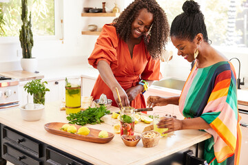 Mature Black women friends cooking together in the kitchen having fun