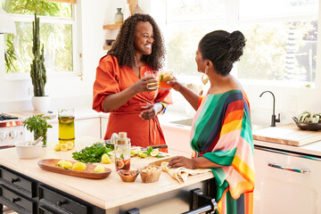 Mature Black friends making a toast with fresh cocktails in kitchen 