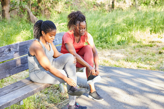 Mature Black women friends tying shoes together in nature for a run