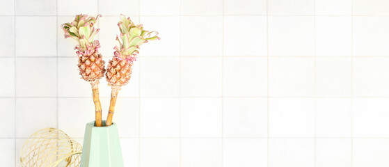 Vase with decorative pineapples near white tile wall. Banner for design