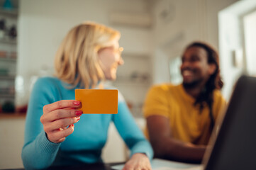 Close up of a woman holding a credit card while shopping online from home and talking to her interracial boyfriend.